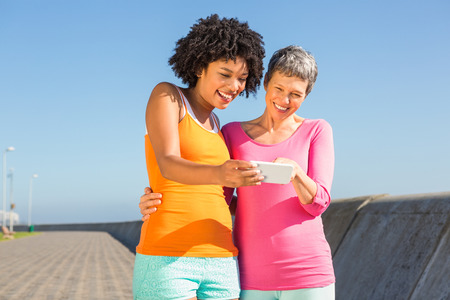 Two smiling sporty women looking at their selfies at promenadeの写真素材