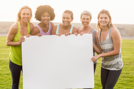 Portrait of smiling sporty women holding poster with copy space in parklandの写真素材