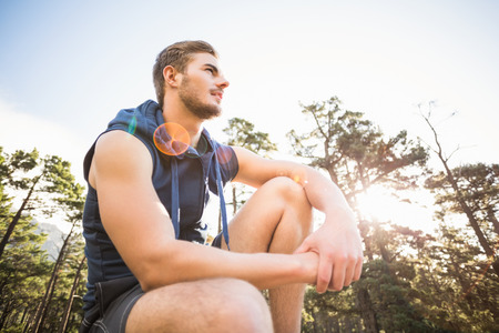 Young happy jogger sitting on rock and looking away in the natureの写真素材
