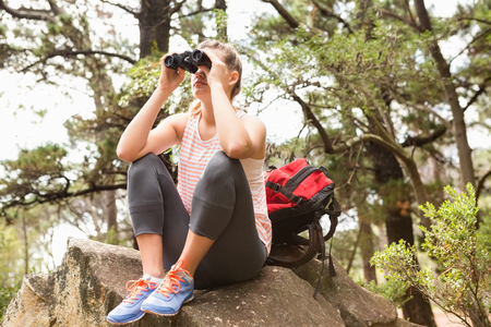 Blonde hiker sitting on rock and  looking through binoculars in the natureの写真素材