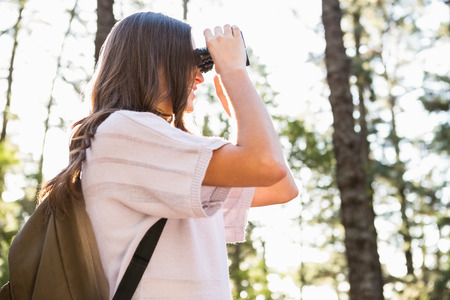 Smiling brunette hiker looking through binoculars in the natureの写真素材