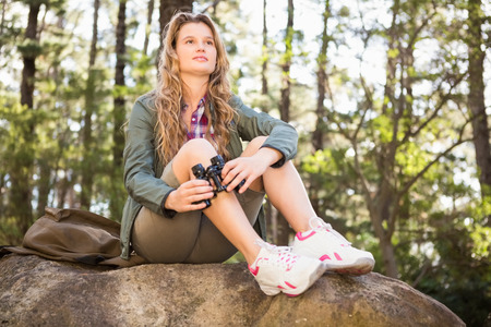 Pretty blonde hiker with binoculars sitting on stone in the natureの写真素材
