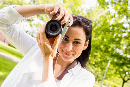 Beautiful brunette taking photo in the park on a sunny day