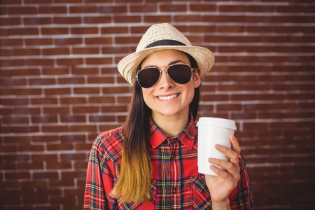 Beautiful hipster with disposable coffee on red brick backgroundの写真素材