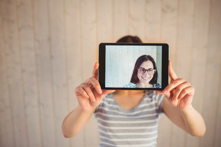 Pretty hipster taking selfie with tablet on wooden planks backgroundの写真素材