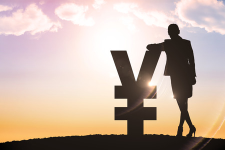 Silhouette beside yen symbol against sun shiningの写真素材