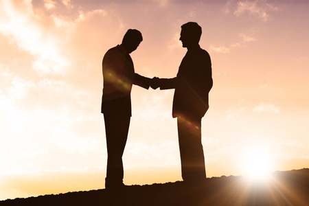 Silhouettes shaking hands against sun shiningの写真素材