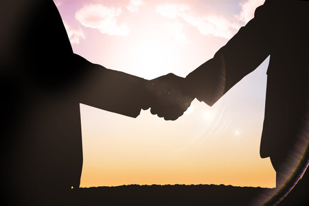Silhouettes shaking hands against sun shiningの写真素材