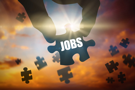 The word jobs and hand holding jigsaw piece against blue and orange sky with cloudsの写真素材