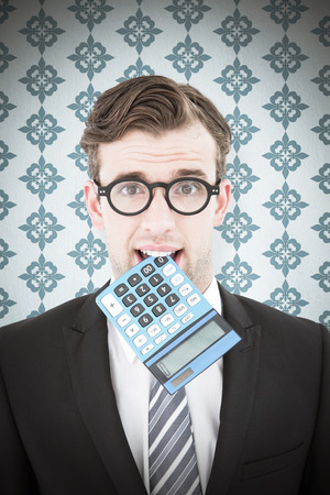 Geeky businessman biting calculator against blue backgroundの写真素材
