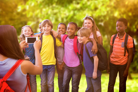 Cute pupils using mobile phone  against trees and meadow in the parkの写真素材