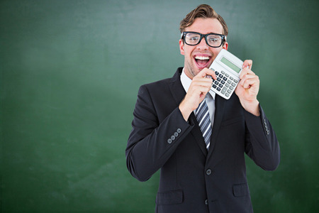 Geeky businessman pointing to calculator  against green chalkboardの写真素材