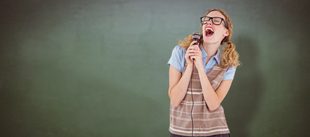 Geeky hipster woman singing into a microphone  against green chalkboardの写真素材