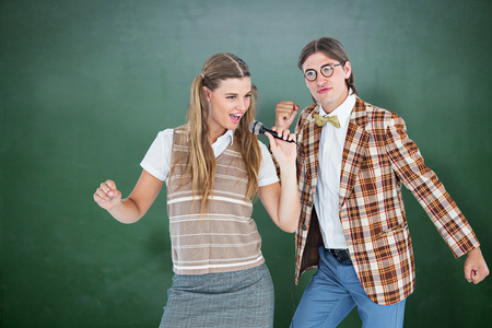 Happy geeky hipsters singing with microphone against green chalkboardの写真素材