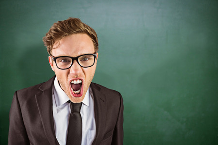 Young angry businessman shouting at camera against green chalkboardの写真素材