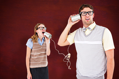 Geeky hipster couple speaking with tin can phone  against deskの写真素材