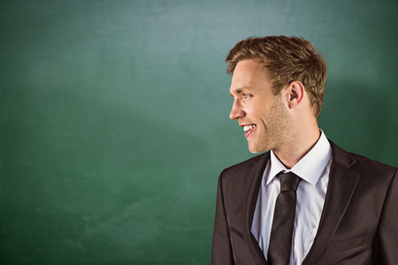 Young handsome businessman looking away against green chalkboardの写真素材