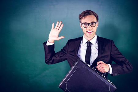 Young geeky businessman holding briefcase against green chalkboardの写真素材