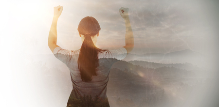 Depressed woman standing back to camera against trees and mountain range against cloudy skyの写真素材