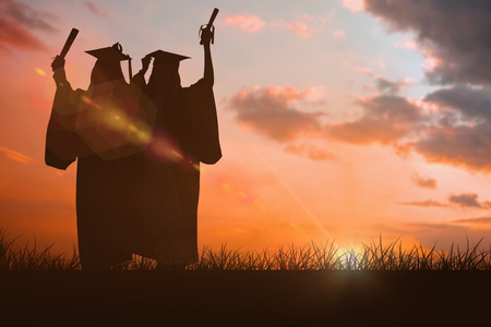 Two women celebrating their graduation against orange and blue sky with cloudsの写真素材