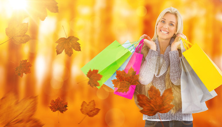 Blonde in winter clothes holding shopping bags against view of a forest in the mistの写真素材