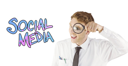 Geeky businessman looking through magnifying glass against social mediaの写真素材