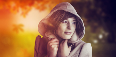 Beautiful woman wearing winter coat looking away against autumn sceneの写真素材