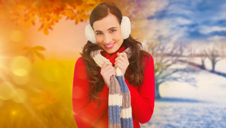 Happy brunette in winter clothes smiling at camera  against autumn changing to winter