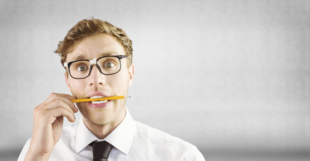 Geeky businessman biting a pencil against grey wallの写真素材