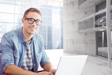 Hipster on laptop against modern room overlooking city