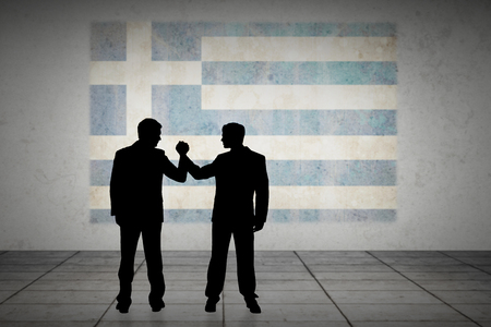 Silhouettes shaking hands against greece flag in grunge effectの写真素材