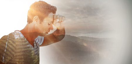 Upset man leaning on white background against trees and mountain range against cloudy sky