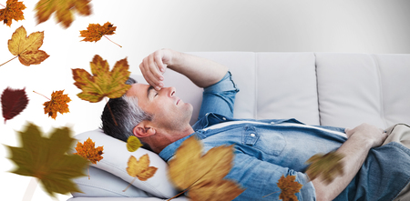 Man suffering from headache while on sofa against autumn leavesの写真素材