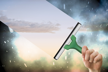 Hand using wiper against cloudy sky with snow falling