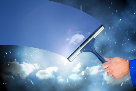 Hand using wiper against cloudy sky with snow falling
