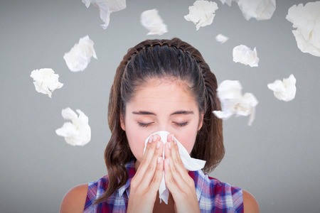 Close-up of sick woman sneezing in a tissue against grey backgroundの写真素材