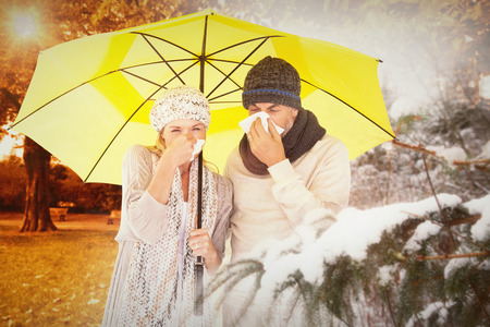 Couple sneezing in tissue while standing under umbrella against trees and meadow in the parkの写真素材