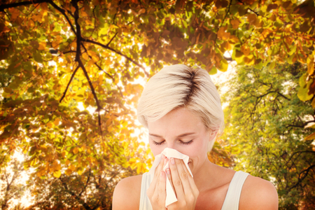 Sick woman blowing her nose against branches and autumnal leaves against the sunlightの写真素材