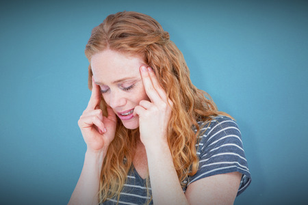 Upset blonde woman suffering from headache against blue backgroundの写真素材
