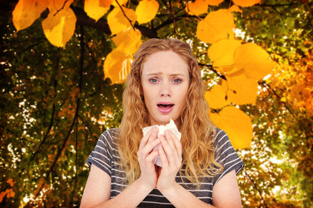 Sick woman sneezing in a tissue against autumnal leaves against plantsの写真素材