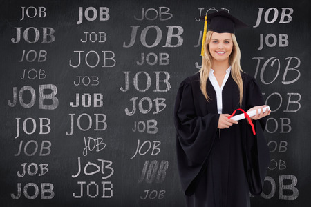Smiling blonde student in graduate robe holding her diploma against blackboardの写真素材