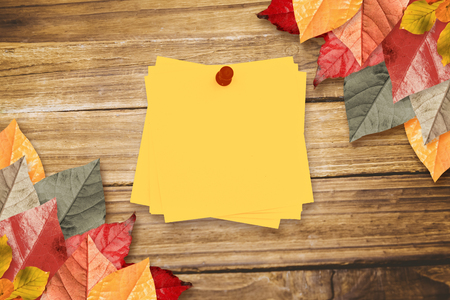 Sticky note with red pushpin against autumn leaves on woodの写真素材