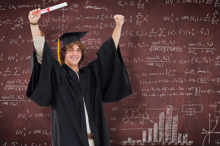 Male student in graduate robe raising his arms against deskの写真素材