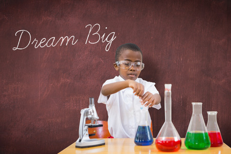 The word dream big and cute pupil playing scientist against deskの写真素材