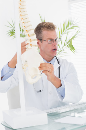Serious doctor showing anatomical spine in clinicの写真素材