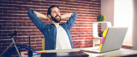 Creative businessman with hands behind back relaxing in office