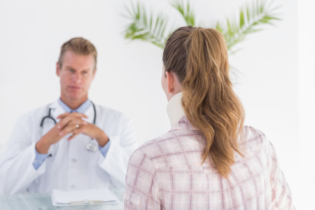 Doctor talking to patient wearing neck brace in medical officeの写真素材
