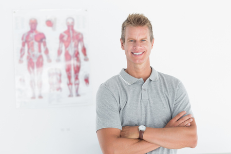 Happy doctor looking at camera with arms crossed in medical officeの写真素材