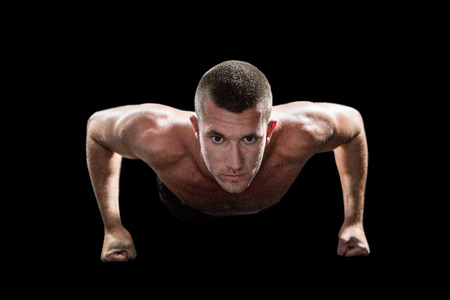 Confident shirtless man doing push ups against black background
