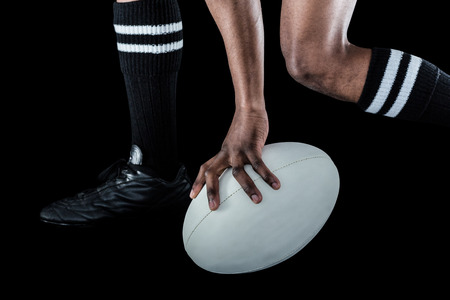 Low section of athlete holding ball while running against black backgroundの写真素材